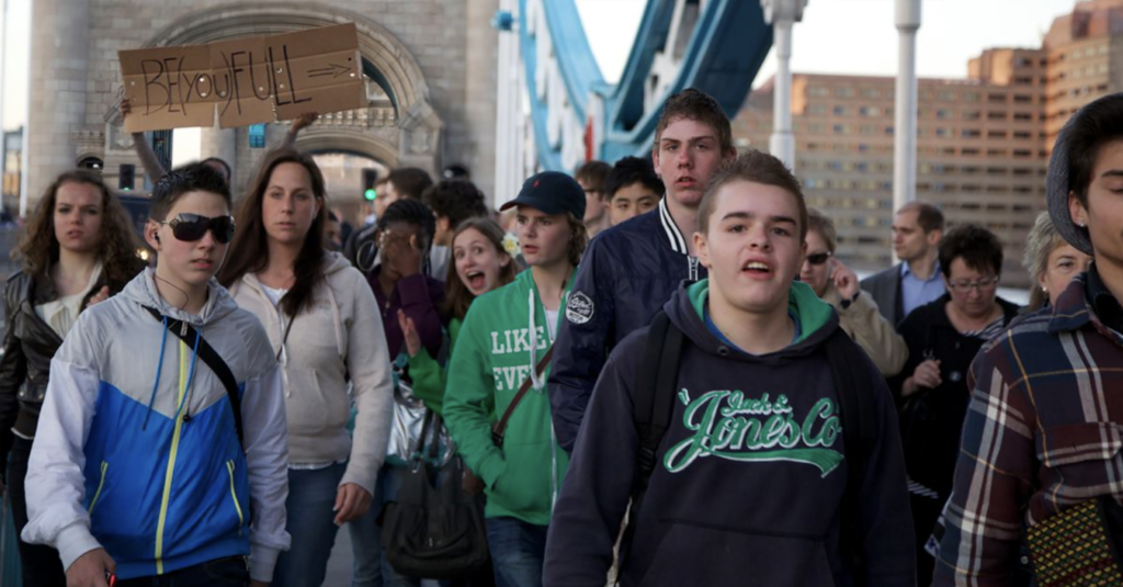 Young people holding a BE(YOU)FULL sign during a public demonstration, promoting education and inclusion.